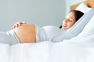Portrait of a cute young pregnant woman lying on bed and looking at her tummy